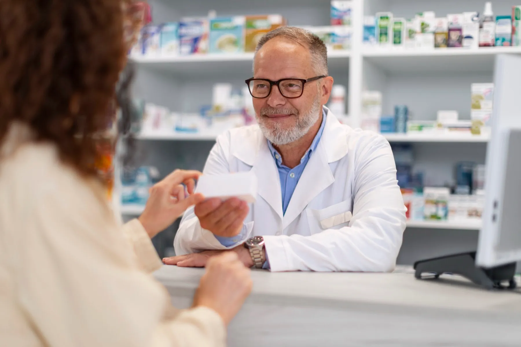 A pharmacist scans a medication package while a customer waits at the counter